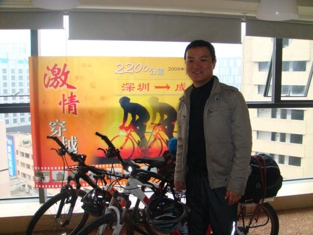 James TJ Lee beside loaded touring bicycles and a poster for the Shenzhen-to-Chengdu ride