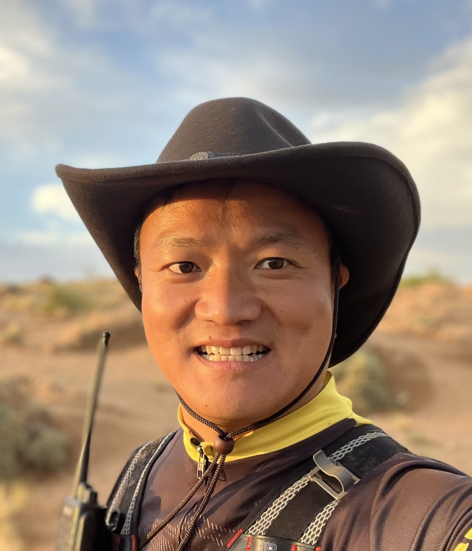 Close portrait of James TJ Lee in a wide-brimmed hat during a desert trek at sunset.
