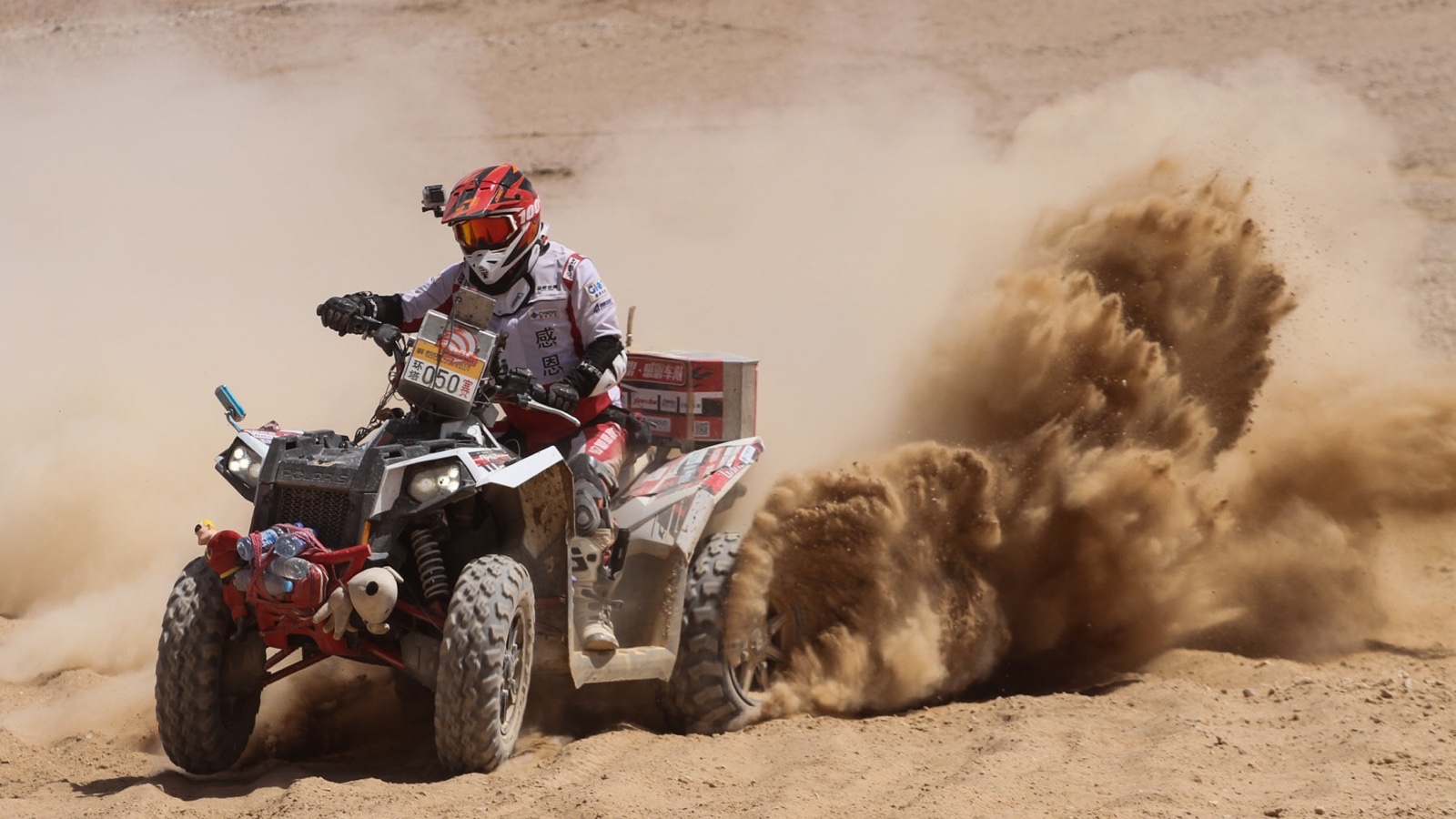 James TJ Lee competing on an ATV in a cross-country rally as sand rises behind him