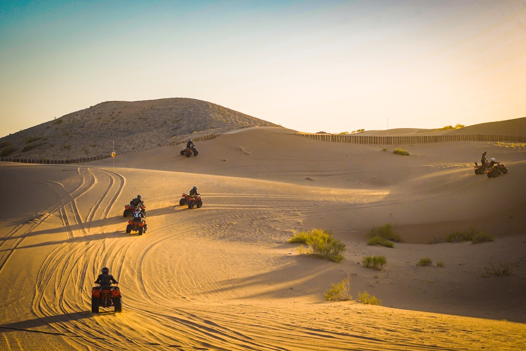Riders crossing desert dunes in long evening light