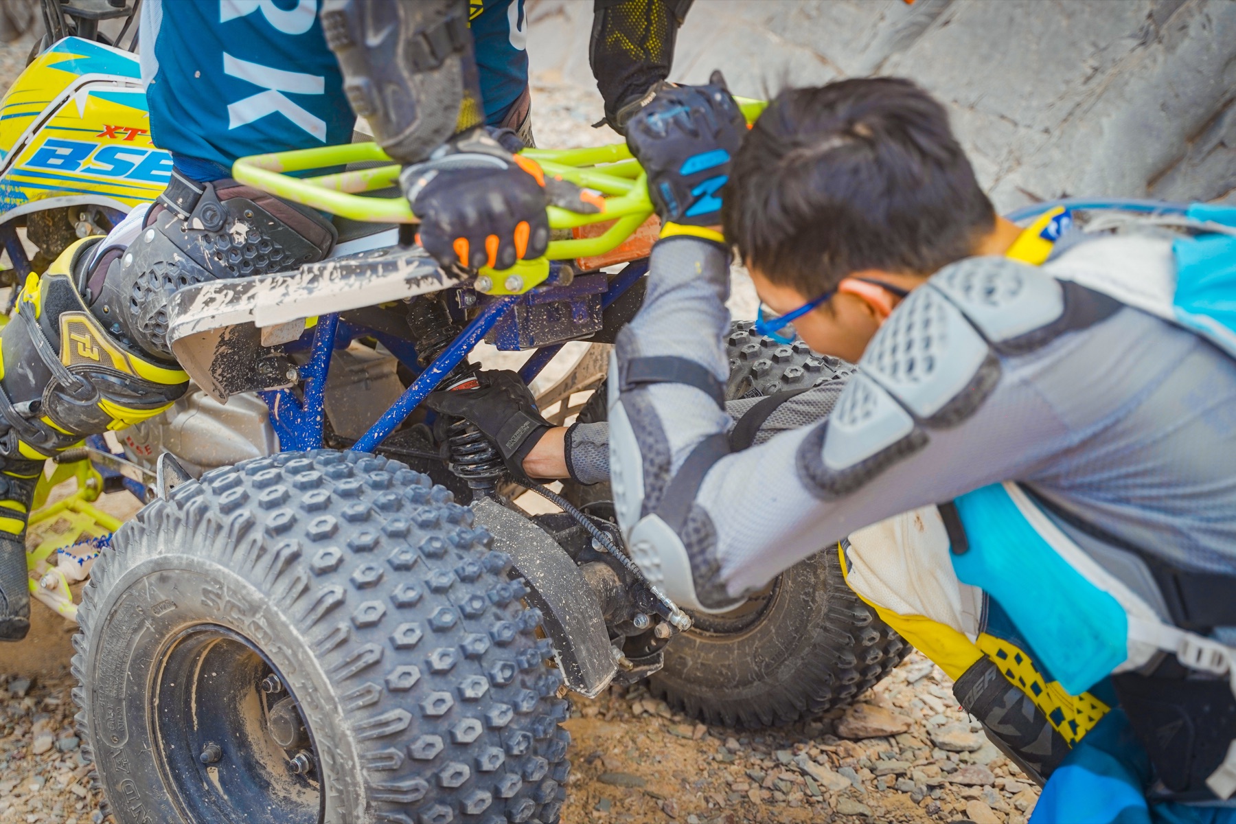 Helmeted Little Knights participants and an adult checking an ATV together on a rocky route